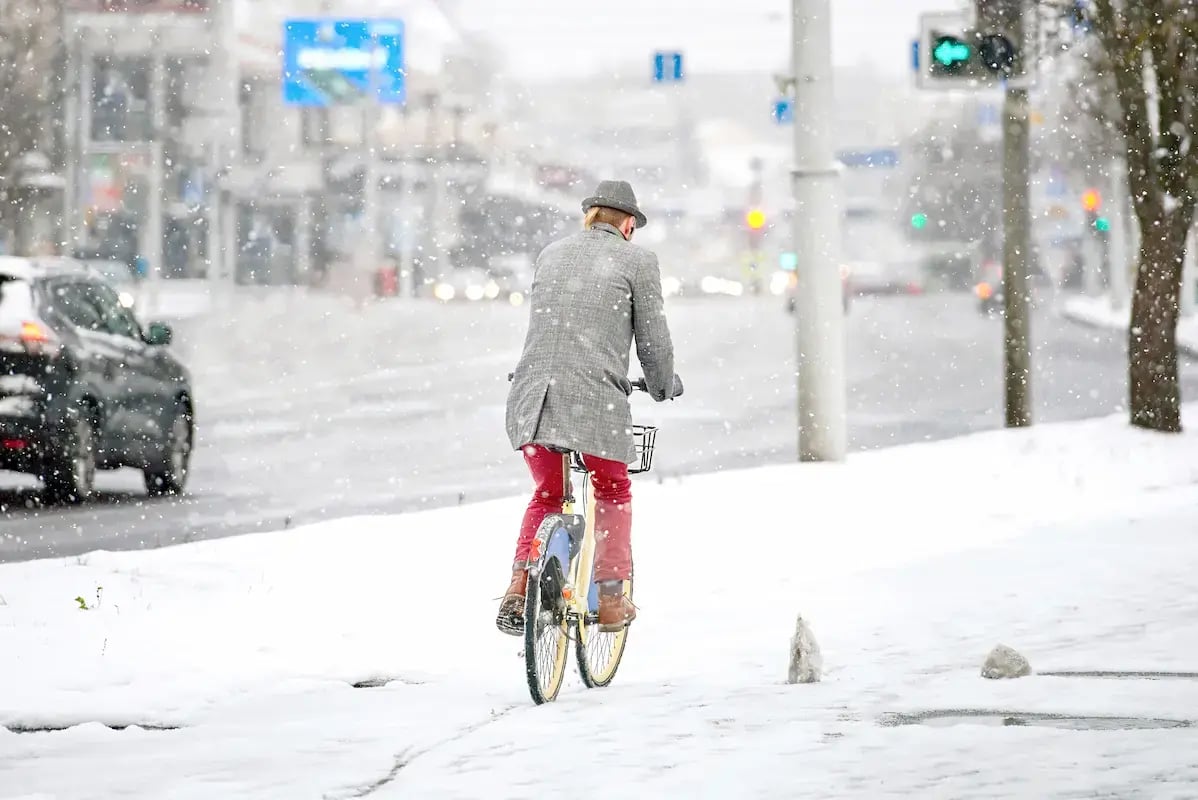 Man in long coat riding bike in the snow