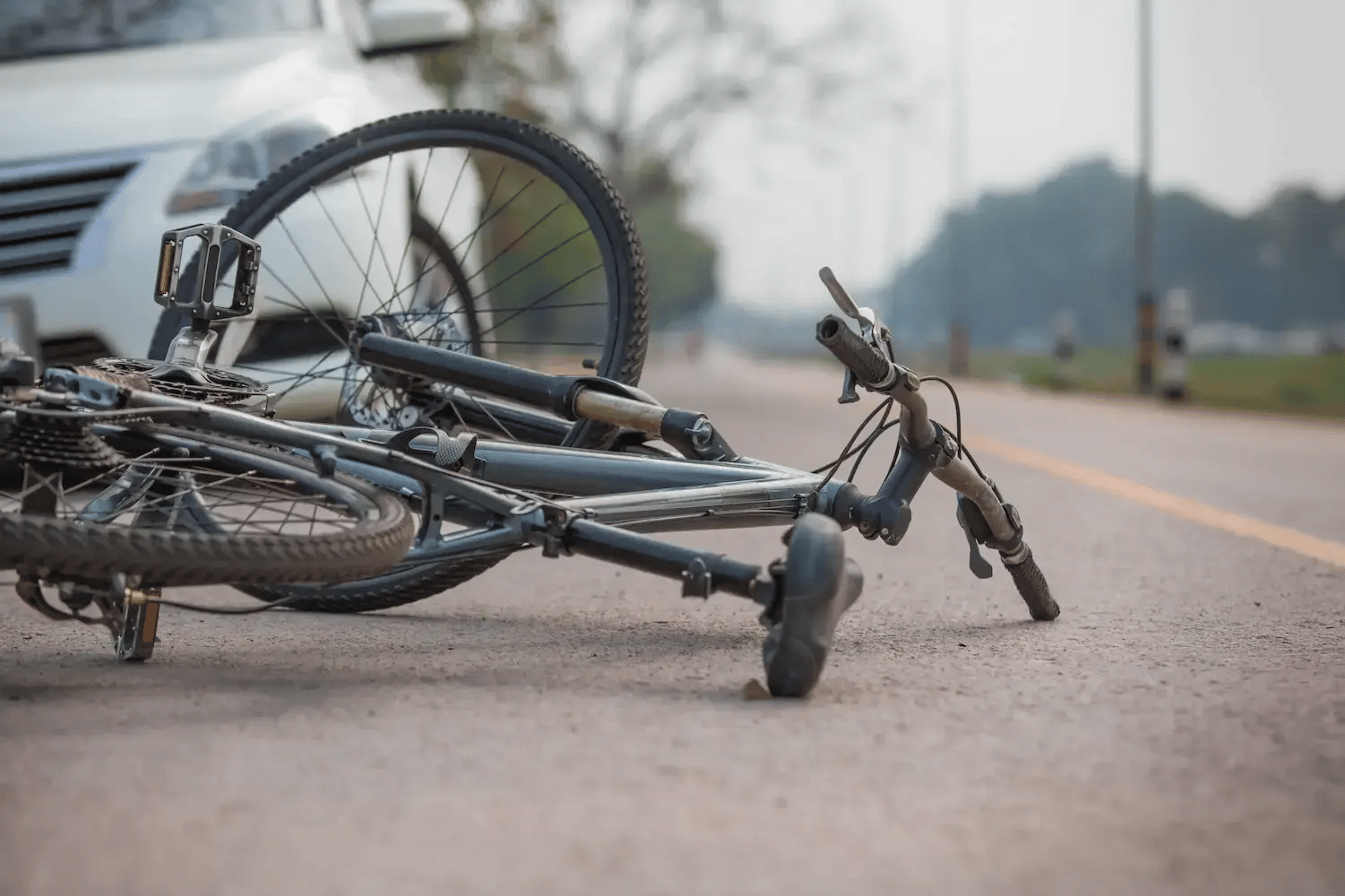 A fallen bike in front of a white car on a road.